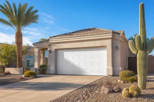 Full exterior view of a residential garage door on an Arizona stucco home with desert landscaping and clear blue sky, illustrating garage door opener remote battery replacement context