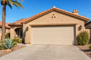 Full exterior view of a residential Arizona home with a two-car traditional steel garage door, desert landscaping and palm trees in bright midday sun